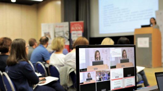 Zdjęcie przedstawiające monitor, na którym wyświetlany jest obraz z kamery rejestrującej szkolenie. W tle uczestnicy szkolenia oraz Paulina Dawidczyk, dyrektor Zespołu ds. Sektora Zdrowia, Zatrudnienia i Szkolnictwa podczas wykładu.